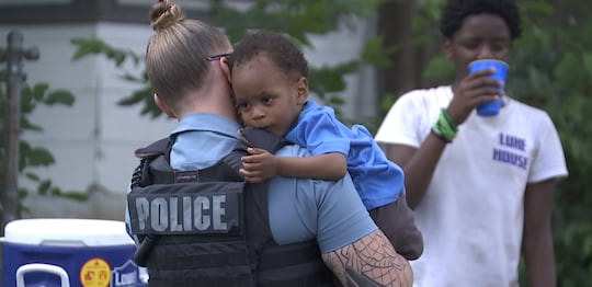 Officer Morgan Reed holds baby at lemonade stand.