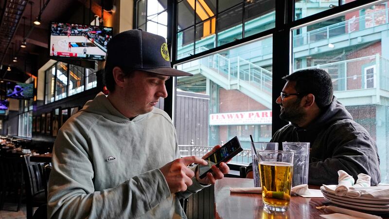 FILE - Taylor Foehl, left, of Boston, looks at the mobile betting app on his phone after...