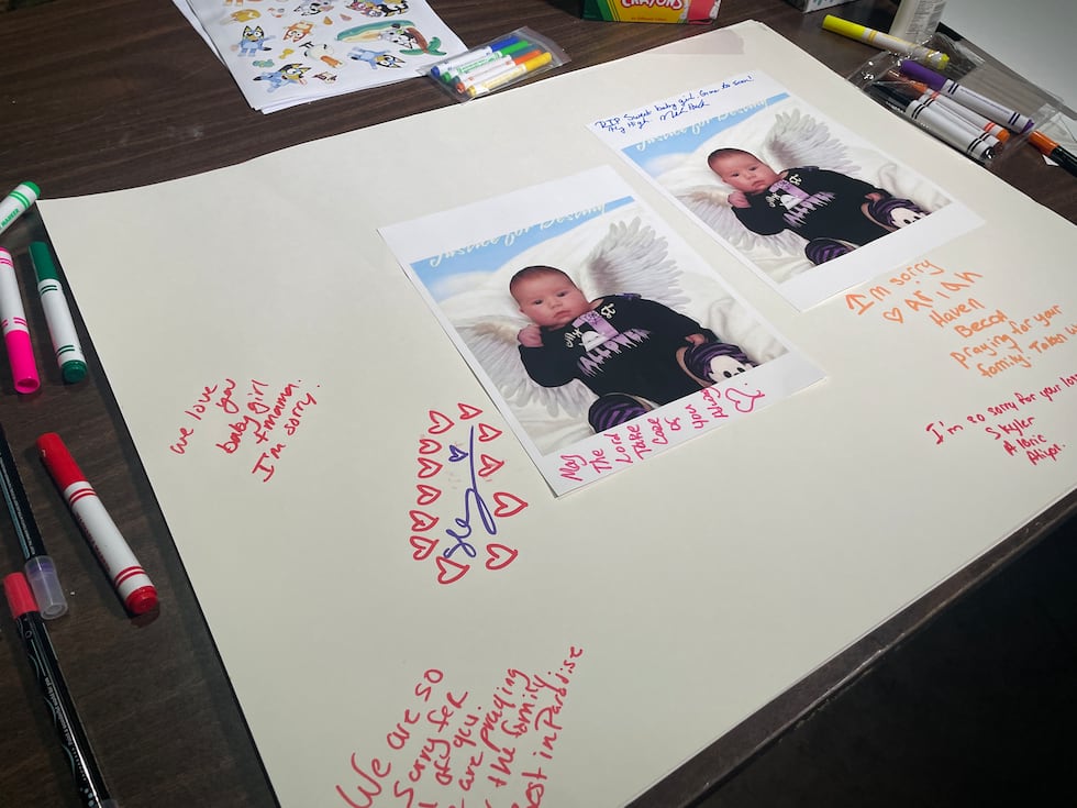 People decorated poster board with photos and messages in marker at a vigil for a mother and...