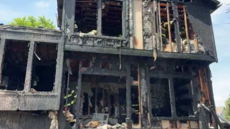 Image shows the back of a two-story house. The windows are broken out and the siding is black...